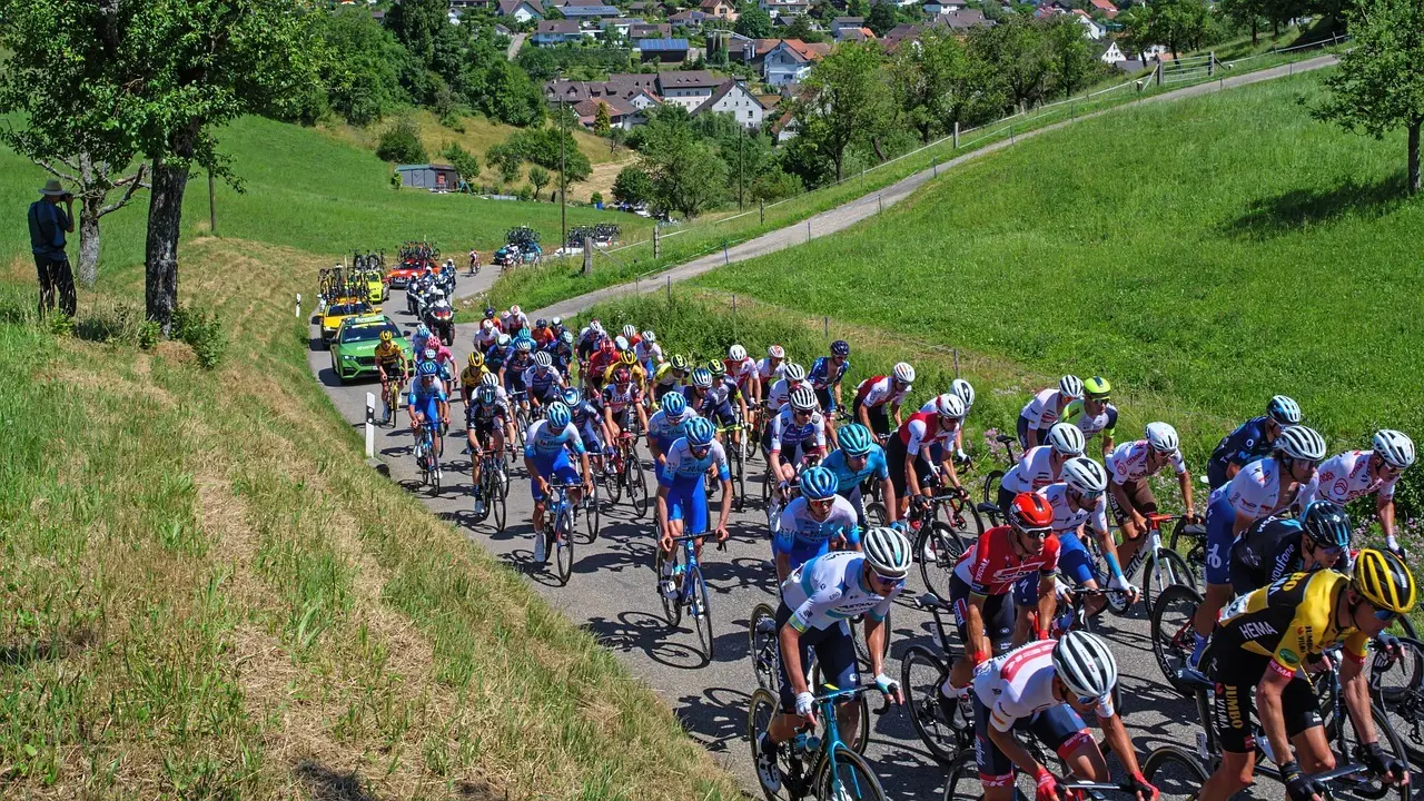 Peloton i landevejsløb med følgebiler og grønt landskab
